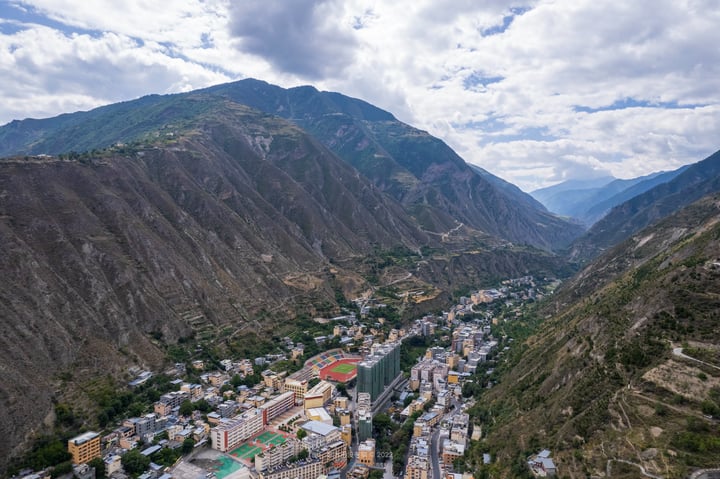 A mountainous valley with a winding road, densely populated with buildings, and a large green mountain in the background.