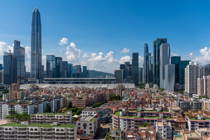 A panoramic cityscape with a mix of modern and older buildings, a tall skyscraper, and a river in the background.