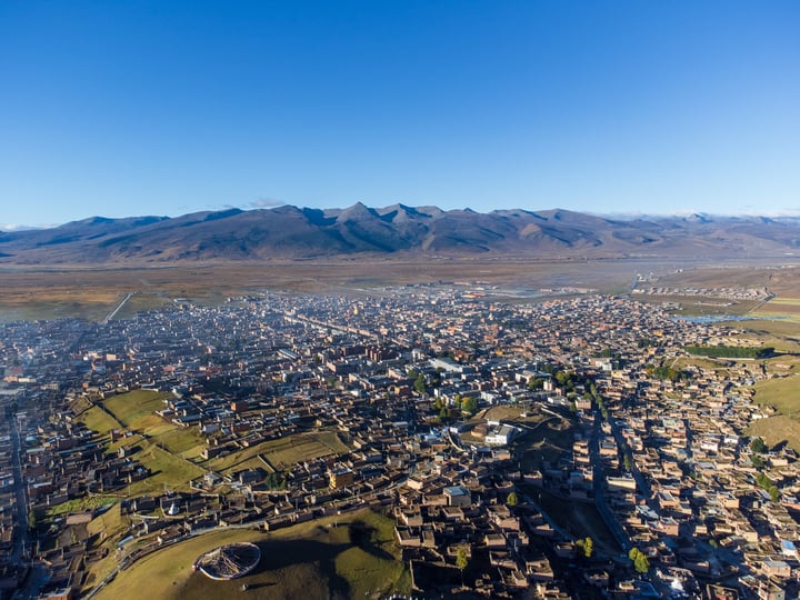 An aerial view of a city nestled between mountains, with a mix of buildings and green spaces, surrounded by snow-capped mountains.