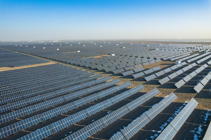 An aerial view of a large solar farm with rows of solar panels in a desert-like environment.