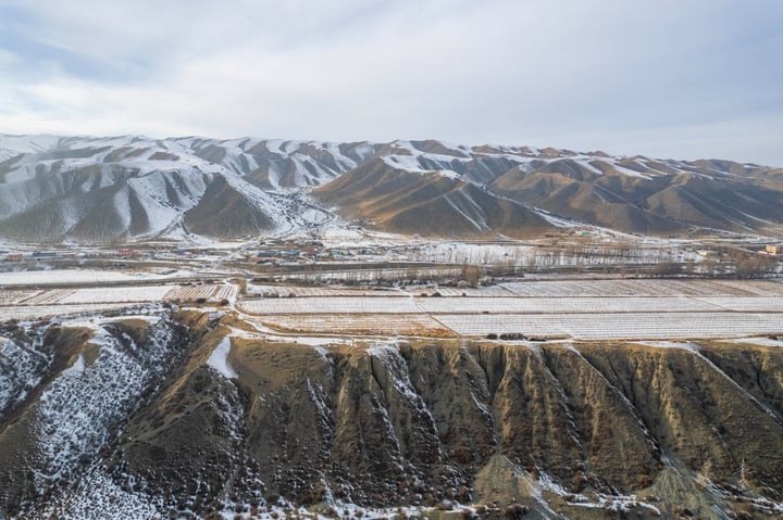A snowy mountain range with patches of greenery, a small town in the valley, and a clear blue sky.