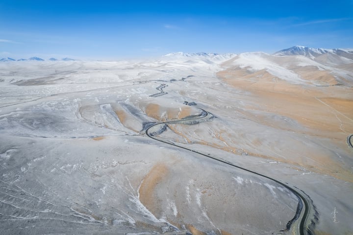 An aerial view of a vast, snow-covered mountain range with a winding road cutting through it.
