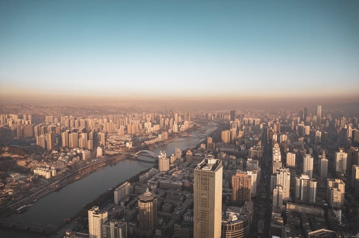 An aerial view of a bustling city with tall buildings, a river, and bridges, all set against a clear blue sky.