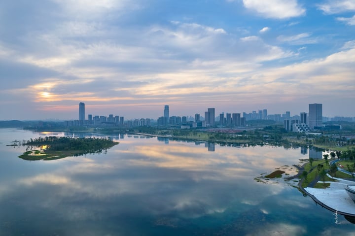 An aerial view of a city with tall buildings, a river, and a park, with a blue sky and clouds.