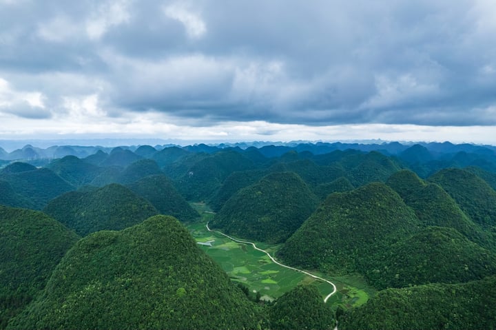 An aerial view of a lush, green mountainous landscape with a winding river, surrounded by a cloudy sky.
