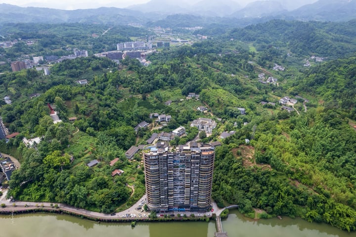 An aerial view of a city nestled between mountains, with tall buildings and a large white dome in the center, surrounded by lush greenery.