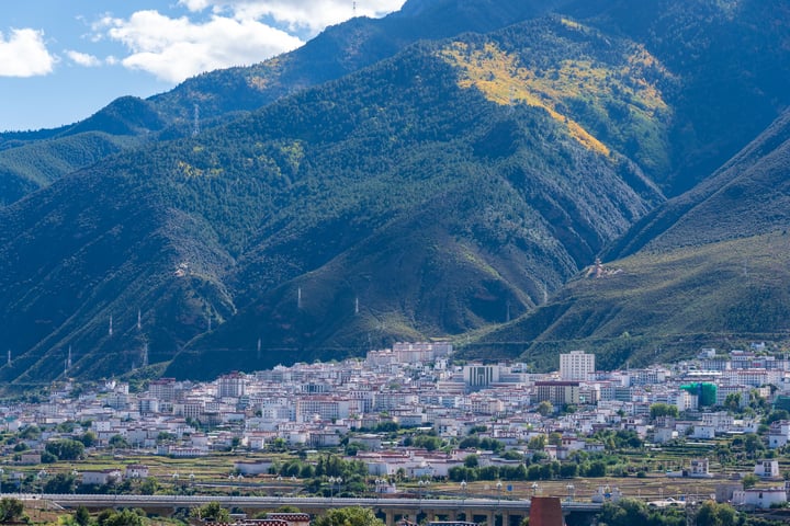 A mountainous landscape with a city nestled amidst greenery, surrounded by a clear blue sky.