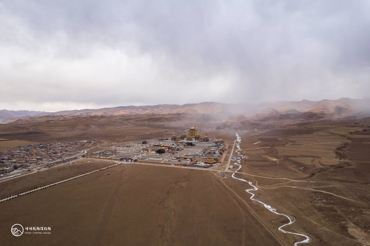 An aerial view of a large oil and gas facility surrounded by barren mountains and a winding river, with a cloudy sky overhead.