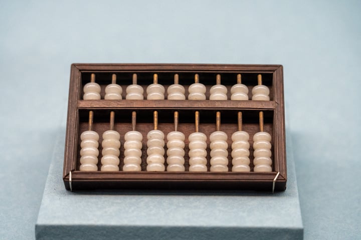 A wooden abacus with 24 wooden beads is placed on a gray surface, with a wooden base and a wooden handle.