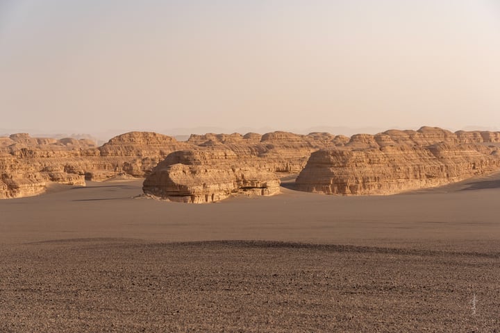 A vast desert landscape features sand dunes and rock formations, with a pale blue sky above.