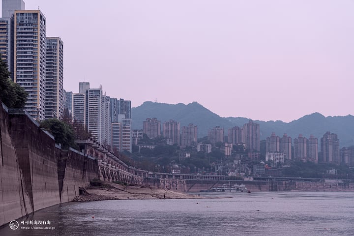 A cityscape with tall buildings, a river, mountains, and a bridge, with a person on a boat.