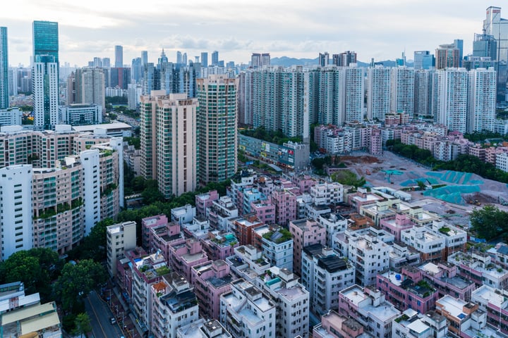 An aerial view of a bustling city with tall buildings, a park, and a basketball court, all set against a cloudy sky.