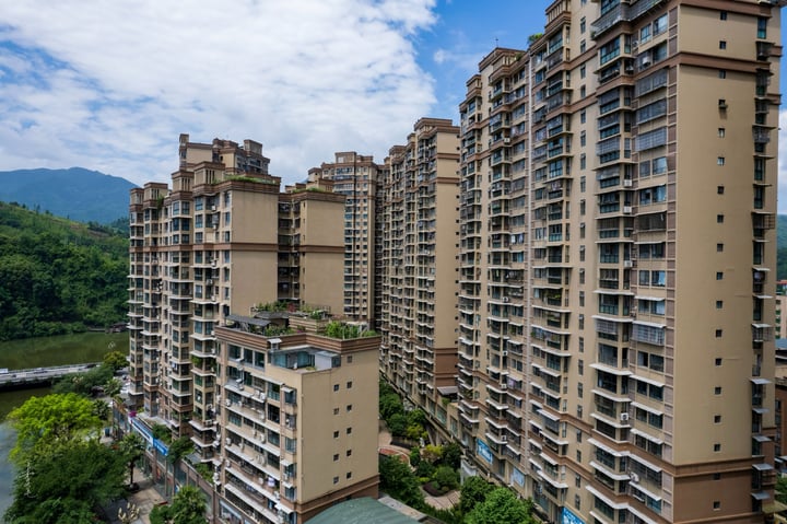 An aerial view of a city nestled between mountains, with tall buildings and a large white dome in the center, surrounded by lush greenery.