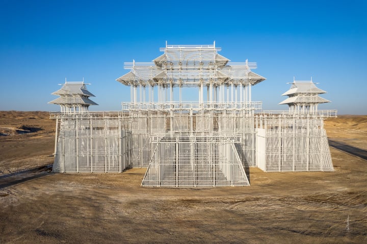 An aerial view of a white, pagoda-like structure with multiple levels and a central roof, surrounded by a barren desert landscape.