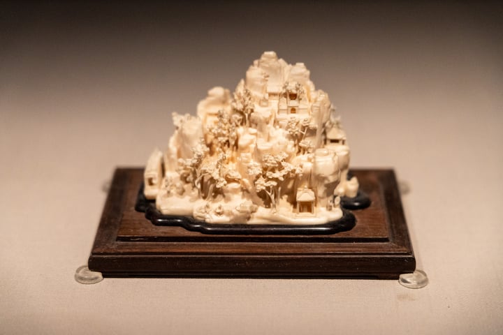 A small, white sculpture of a mountain, with intricate details, is displayed on a wooden stand on a table.