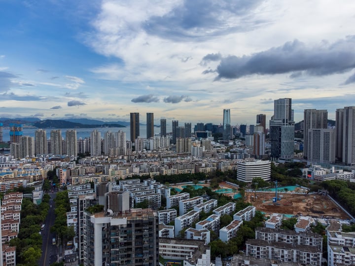 A panoramic view of a bustling city with tall buildings, a large body of water, and mountains in the background.
