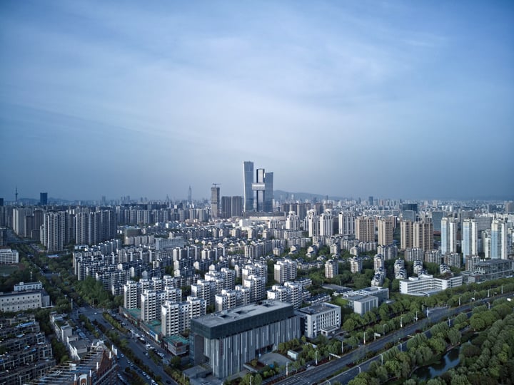 A bustling cityscape with numerous tall buildings, including skyscrapers and a tower, is captured from a high vantage point, showcasing the urban landscape's density and architectural diversity.