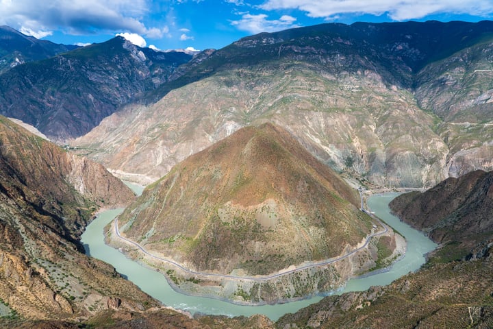 A breathtaking view of a valley with a river winding through it, surrounded by mountains and a blue sky with clouds.