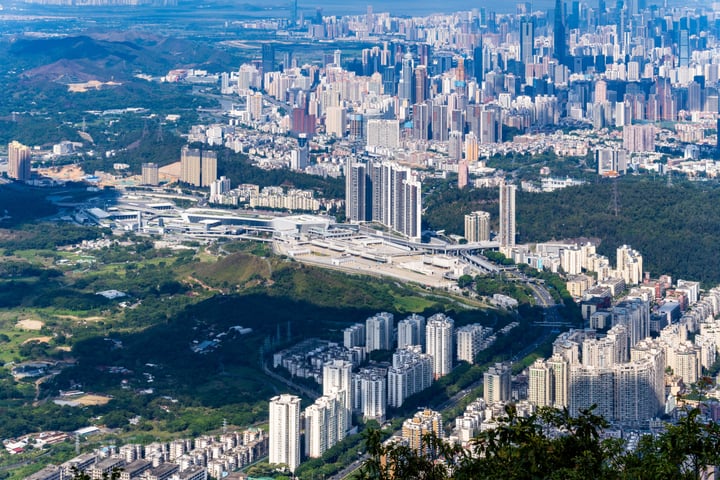 A panoramic view of a bustling city with tall buildings, roads, and highways, surrounded by greenery and mountains, captured from a high vantage point.