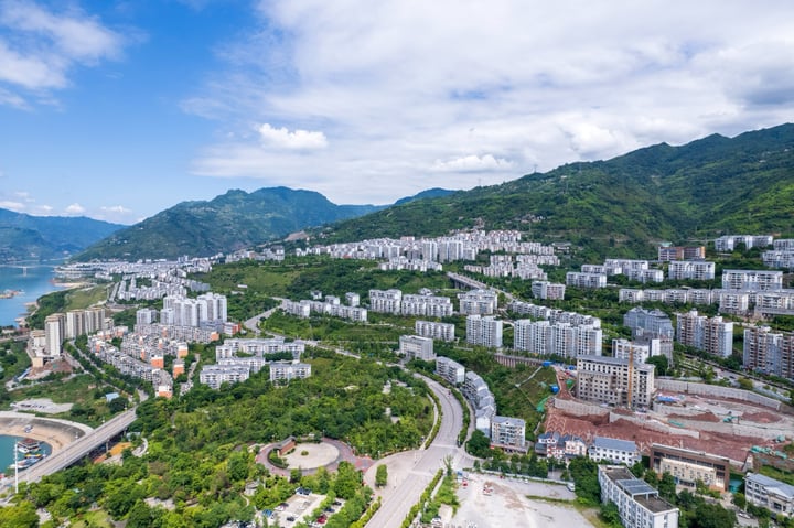 An aerial view of a city nestled between mountains, with a large body of water in the foreground and a cityscape in the background.