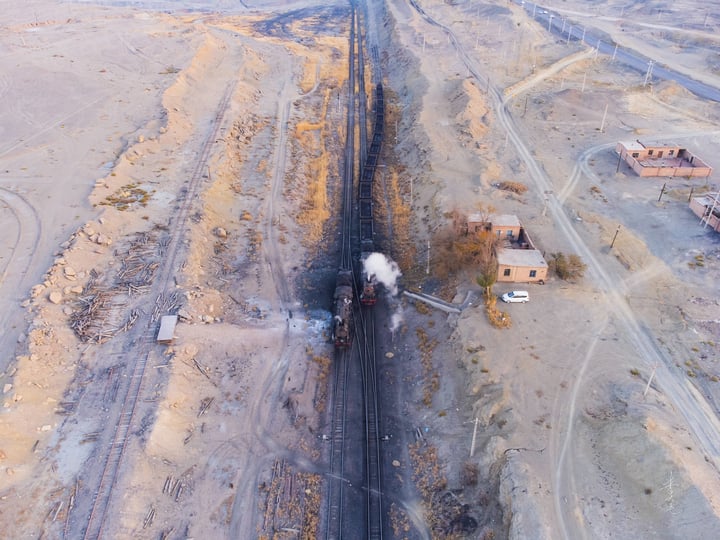 An aerial view of a train track with a train on it, surrounded by a desert and a small building.