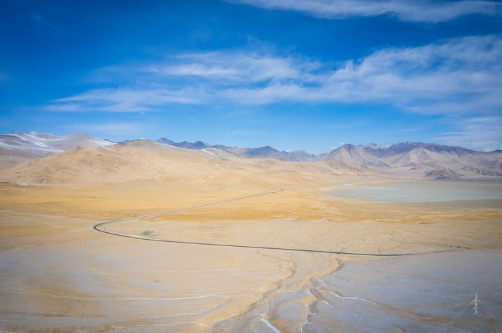 A vast, barren desert landscape with a winding river in the foreground, surrounded by mountains and a clear blue sky.
