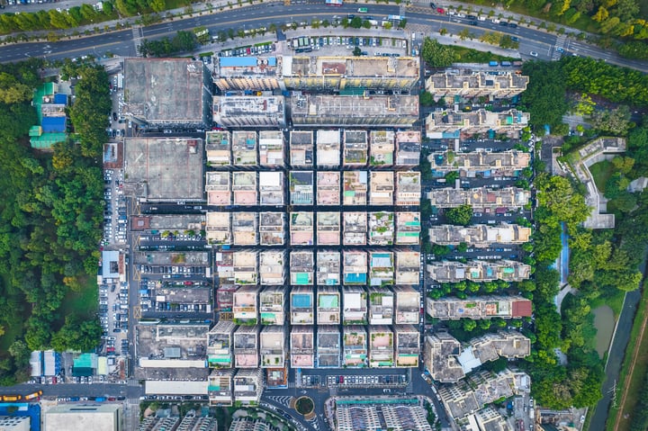 An aerial view of a city with a grid-like layout of buildings, roads, and parks, surrounded by greenery.