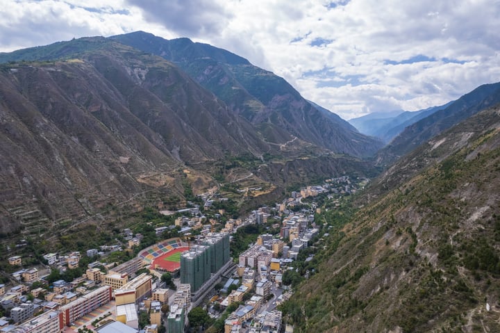 A mountainous valley with a city in the center, surrounded by mountains and greenery, with a football field in the foreground.