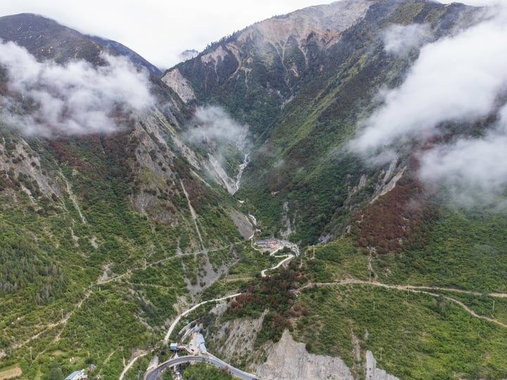 An aerial view of a Deqin County, surrounded by lush greenery and surrounded by mountains. The town is densely populated with houses and buildings, and the roads crisscross the valley. The town is surrounded by trees and hills, creating a serene and picturesque scene.