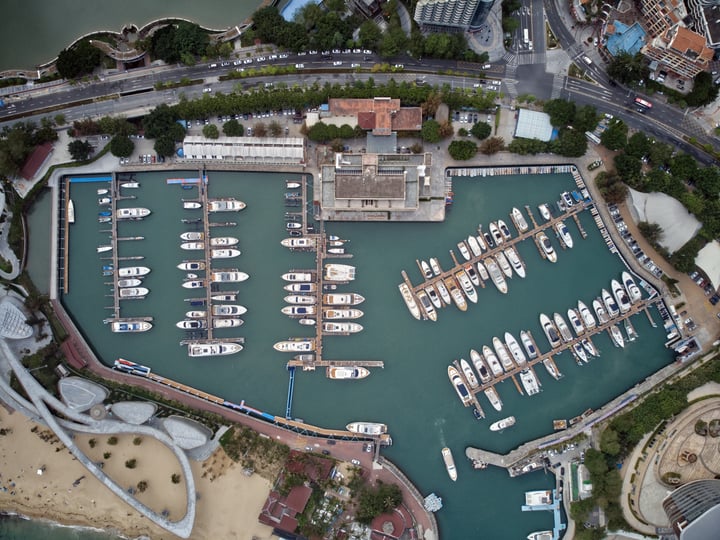 An aerial view of a bustling harbor with numerous boats docked in a large body of water, surrounded by buildings and roads.