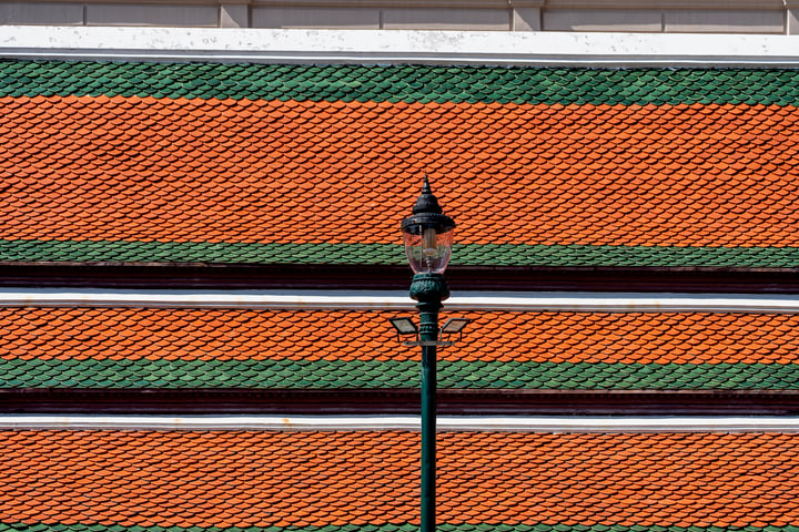 A street lamp stands on a green pole in front of a colorful, orange and green striped building.