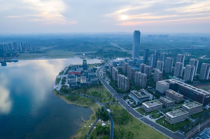 An aerial view of a city with tall buildings, a river, and a park, with a blue sky and clouds.