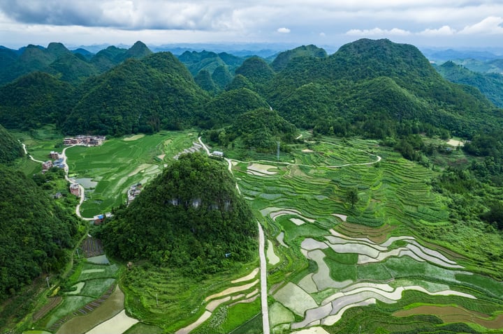 An aerial view of a mountainous region with rice terraces, surrounded by lush greenery and a clear blue sky.