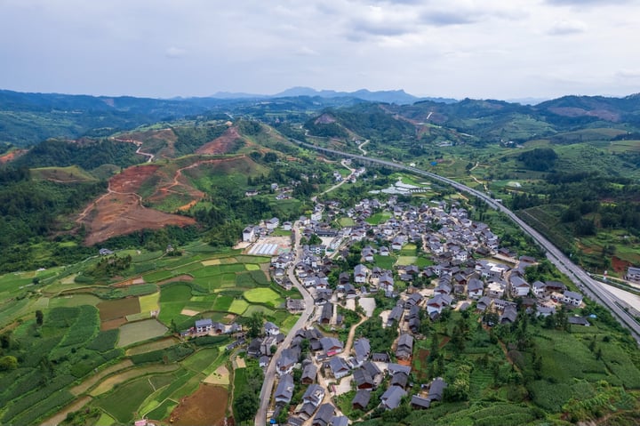 An aerial view of a small town nestled in a valley, surrounded by lush green fields and mountains, with a winding road running through it.
