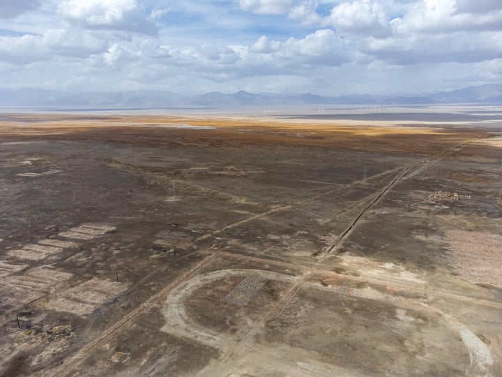 An aerial view of a vast, barren desert landscape with a vast expanse of dirt and sand, dotted with scattered rocks and a few distant mountains.