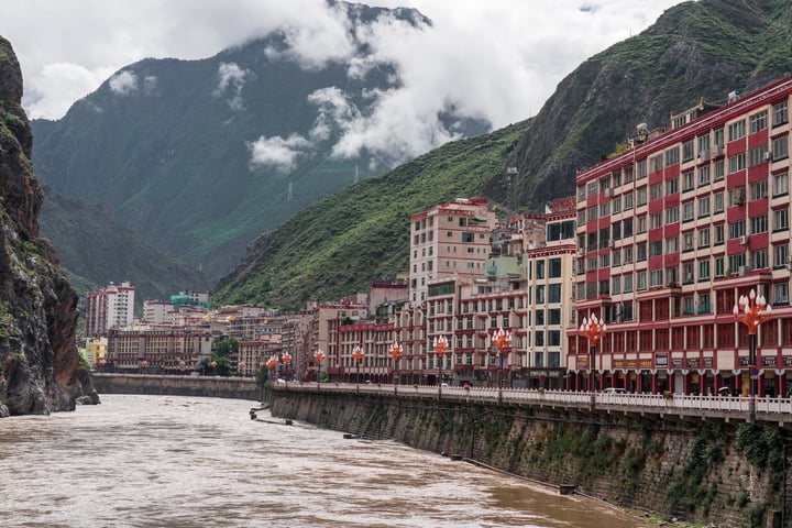 A serene mountainous cityscape with a river, red and white buildings, and a cloudy sky.