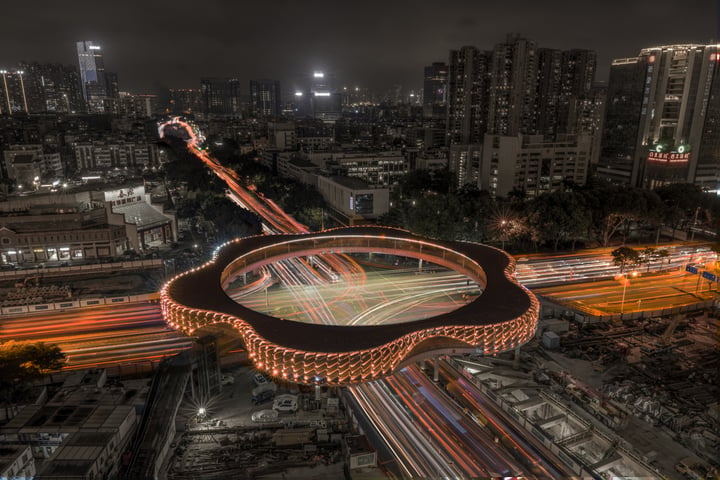 A nighttime cityscape features a circular, illuminated highway with a circular road, surrounded by a dense urban environment.