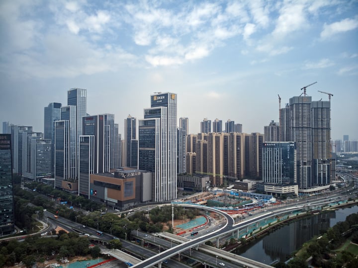 A bustling cityscape with towering skyscrapers, a busy highway, and construction sites is captured in a high-angle view.
