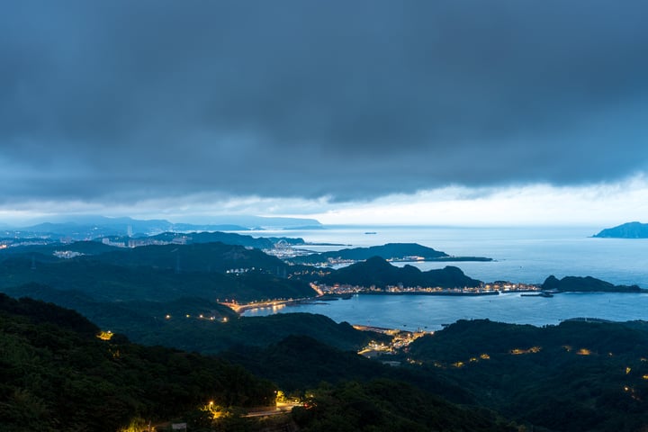 A serene night scene in Japan, with a mountainous landscape, a deep blue ocean, and a cityscape in the distance.