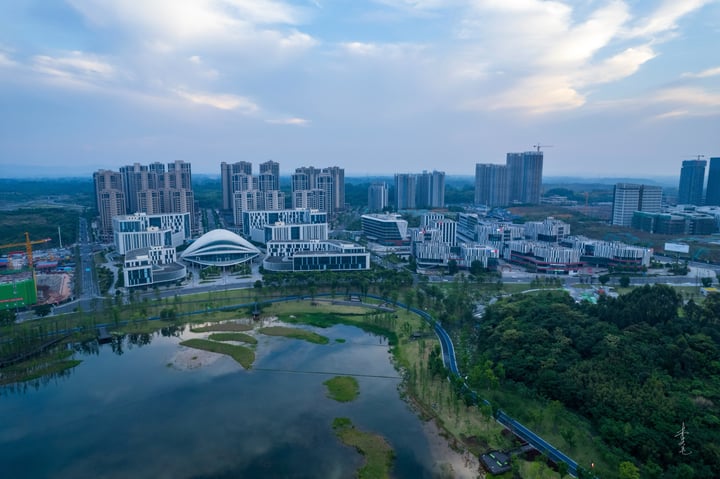 An aerial view of a city with tall buildings, a river, and a park, with a blue sky and clouds.