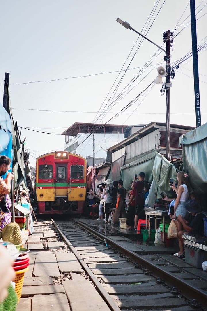 A bustling train station is filled with people waiting to board a colorful train.