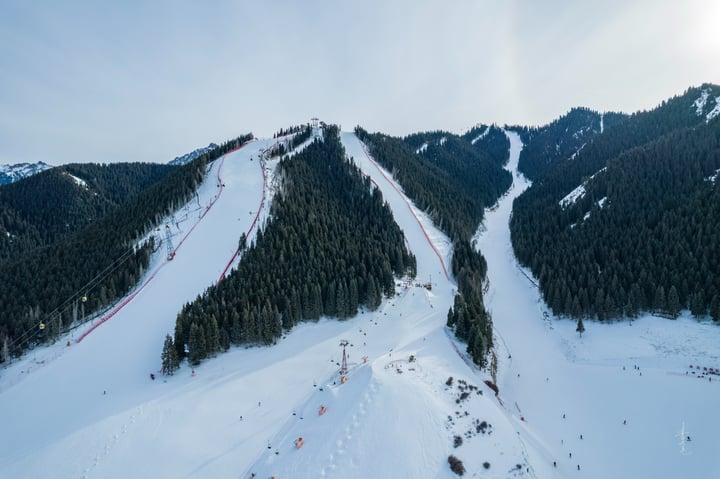 A snowy mountain slope with a red fence, a ski lift, and a vast landscape with snow-covered mountains and trees.