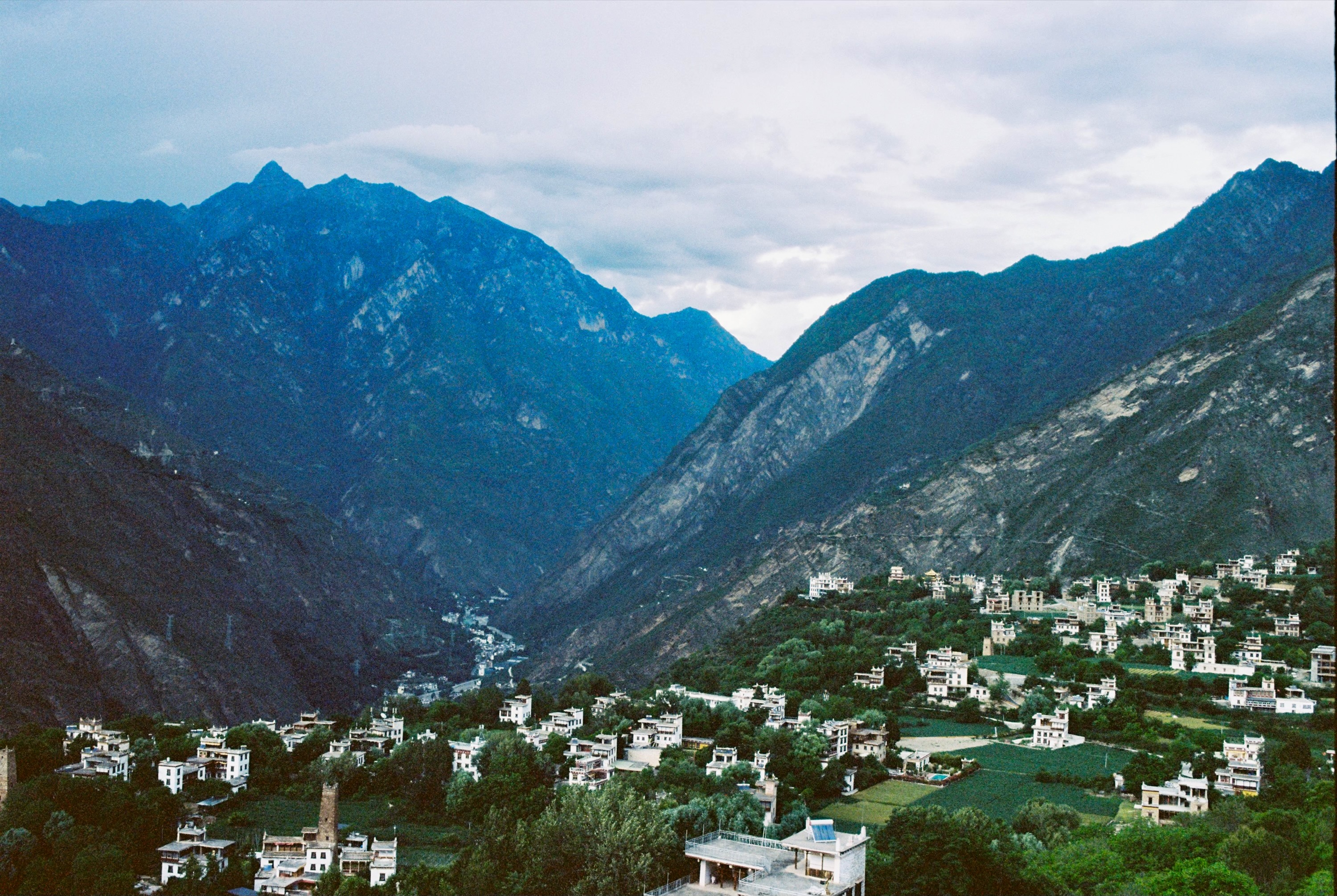 A serene mountainous valley with a winding river, a small town, and a mountain range in the background.