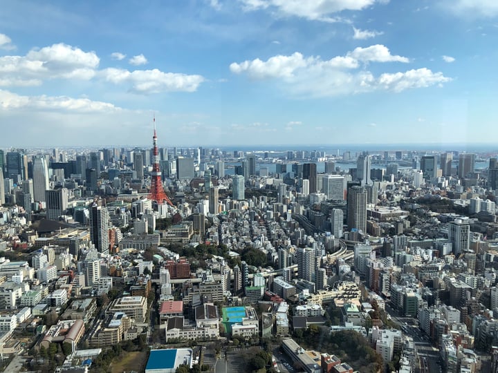 A bustling cityscape with a prominent red and white tower, surrounded by tall buildings and a clear blue sky.