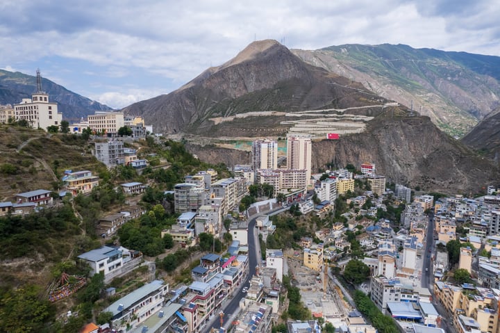 A mountainous cityscape with a mix of buildings, roads, and mountains, with a red "T" sign on one building.