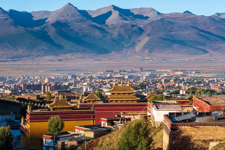 A panoramic view of a mountainous city with a golden temple, surrounded by lush green trees and a clear blue sky.
