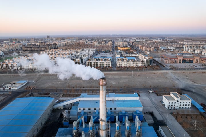 An aerial view of a large industrial complex with multiple buildings, including a large factory with smokestacks and a large factory with a large factory. The complex is surrounded by a large city with buildings of varying heights and colors. The sky is clear with a few clouds.
