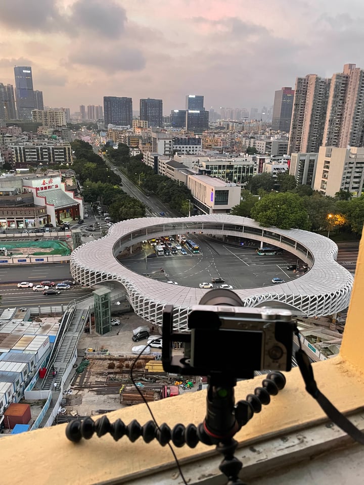A cityscape view from a high-rise building with a panoramic view of a parking lot filled with cars and a large circular building in the center.