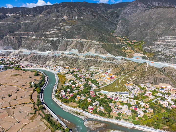An aerial view of a picturesque valley with a winding river, surrounded by mountains and houses, with a small town in the valley.