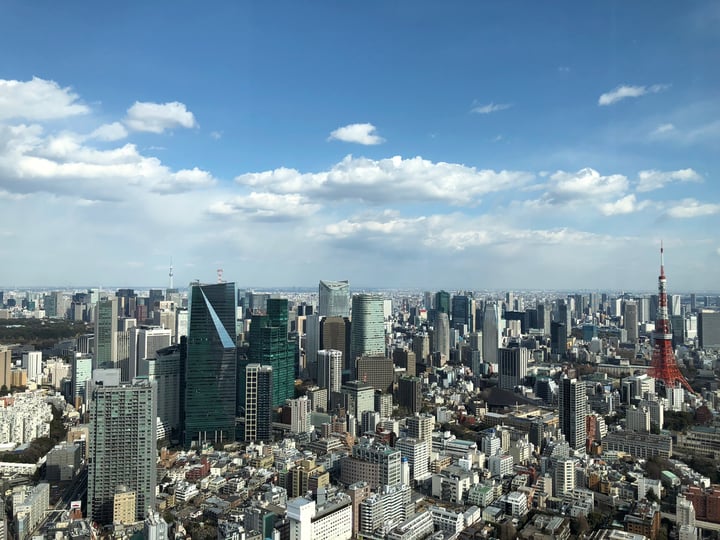 A bustling cityscape with numerous skyscrapers, a prominent red and white tower, and a clear blue sky.